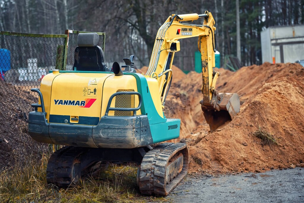 На фотографії зображено невеликий гусеничний екскаватор марки Yanmar, що працює на будівельному майданчику.