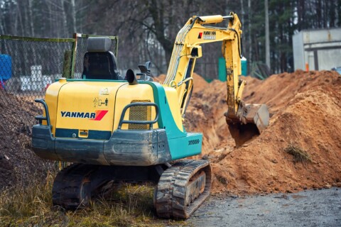 На фотографії зображено невеликий гусеничний екскаватор марки Yanmar, що працює на будівельному майданчику.