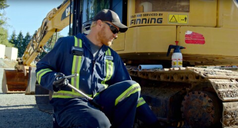 Механік у робочому одязі з інструментом у руці, який ремонтує будівельну машину марки CAT.