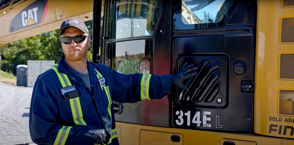 Механік у захисному одязі стоїть біля екскаватора CAT 314E L на будівельному майданчику.