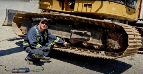 Механік у робочому одязі, що стоїть на колінах біля гусениці будівельної машини, перевіряє систему ходової частини.