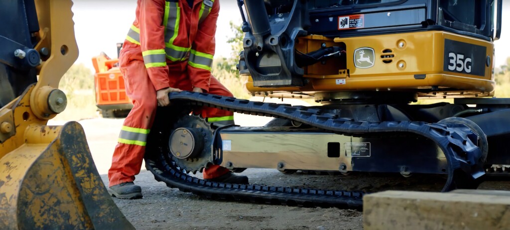 Технік, який встановлює гумові гусениці на будівельній машині John Deere 35G.