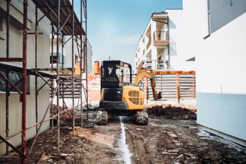 Маленький екскаватор на гумових гусеницях, що працює на будівельному майданчику між житловими будинками.