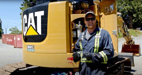 Чоловік у робочому одязі стоїть перед будівельною машиною марки CAT.