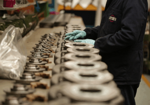 Працівник у темному комбінезоні та рукавичках складає металеві деталі.