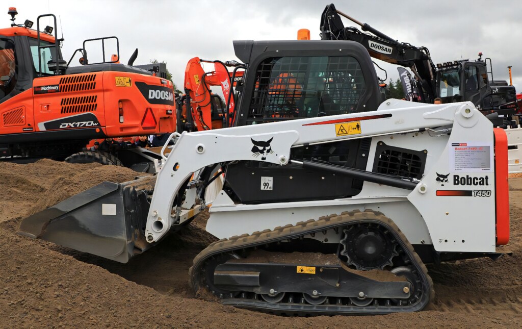 Компактний гусеничний навантажувач Bobcat T450, що працює на будівельному майданчику, на тлі будівельних машин марки Doosan.