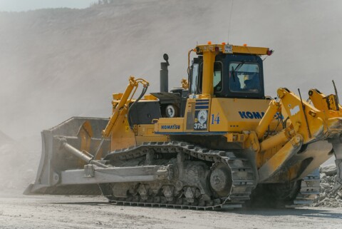 Бульдозер Komatsu D375A на гусеничному шасі працює на будівельному майданчику в запиленому середовищі.