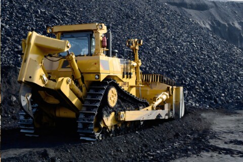 Жовтий гусеничний бульдозер, що працює на великому вугільному відвалі.