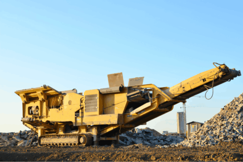 Щелепна дробарка, що працює на майданчику, з великою купою заповнювача на задньому плані.