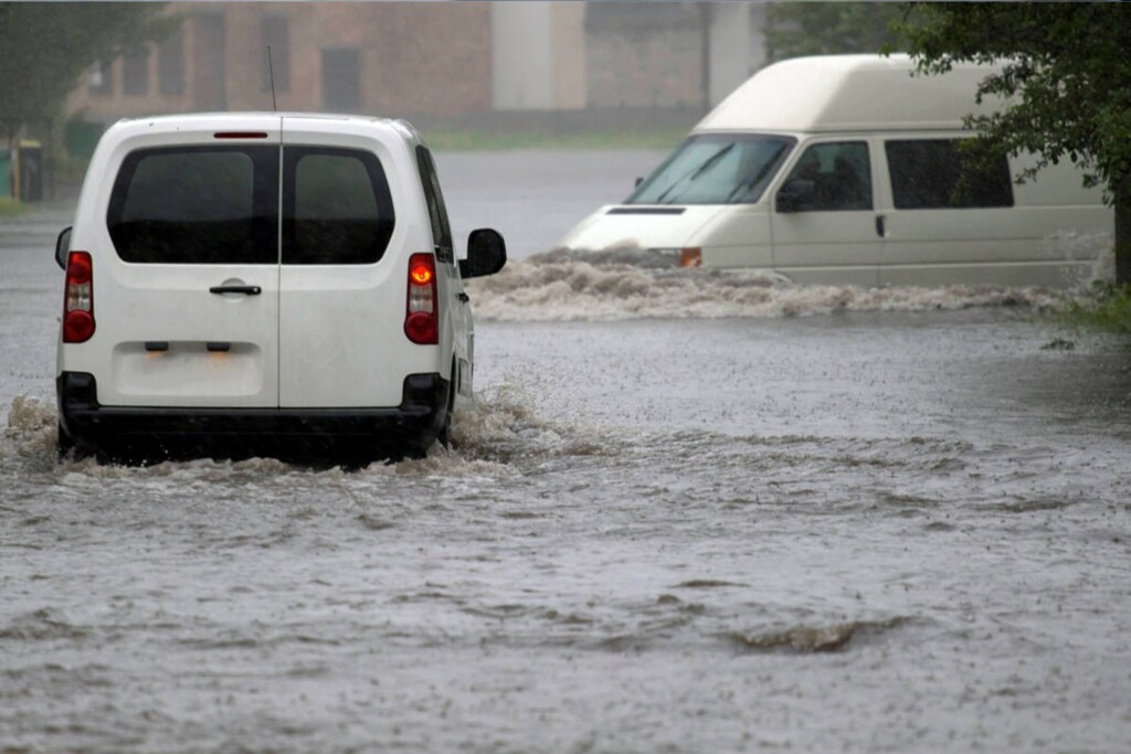 Два білих мікроавтобуси рухаються по затопленій дорозі.