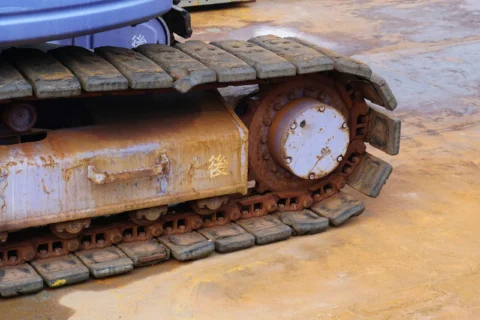 Зношені гумові гусениці та ведуче колесо міні-екскаватора з видимими ознаками корозії від польових робіт.