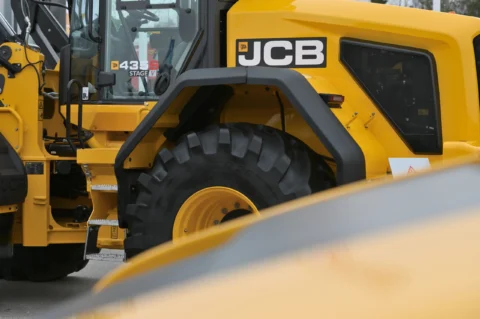 Крупний план жовтого екскаватора JCB з видом на колесо та кабіну оператора.