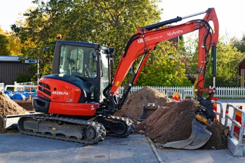 Міні-екскаватор Kubota на гусеничному ходу, що виконує земляні роботи при викопуванні на забудованій території.